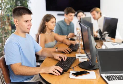 Guy student of computer courses looks at monitor screen, types on keyboard and Stock Photos