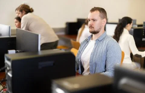 Guy student of computer courses looks at monitor screen, types on keyboard and 스톡 사진