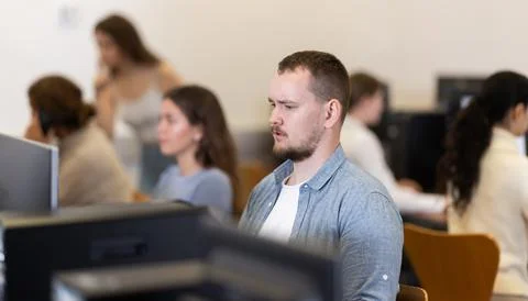 Guy student of computer courses looks at monitor screen, types on keyboard and Stock Photos