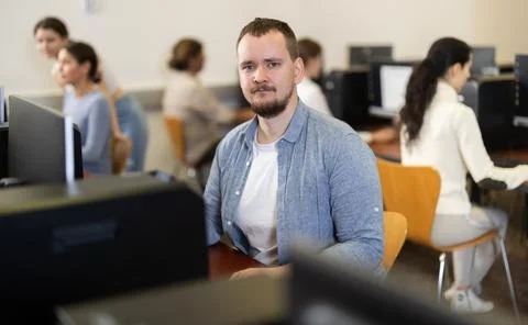 Guy student of computer courses looks at monitor screen, types on keyboard and Stock-Fotos