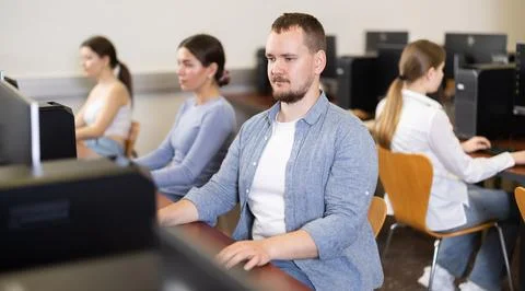 Guy student of computer courses looks at monitor screen, types on keyboard and Stock Photos