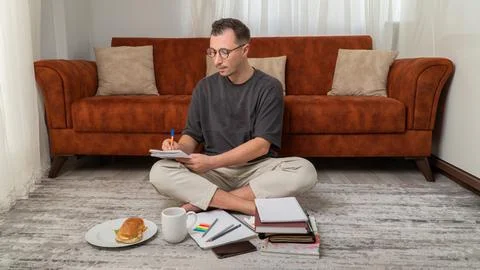 A guy student to study at home, writes in notebooks with books and textbooks Stock Photos