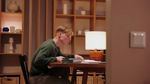 Guy studying at home, having a video call on a laptop, searches through textbook 스톡 동영상 164380345