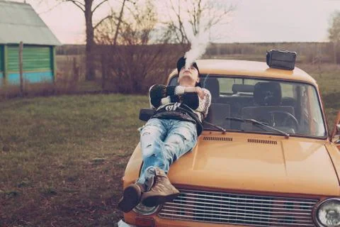 Guy in the style of the nineties smokes lying on the hood of the car Stock Photos