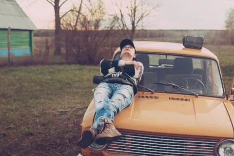 Guy in the style of the nineties smokes lying on the hood of the car Stock Photos