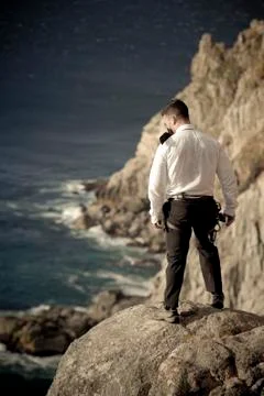 Guy in suit standing on edge of ocean cliff rock Stock Photos