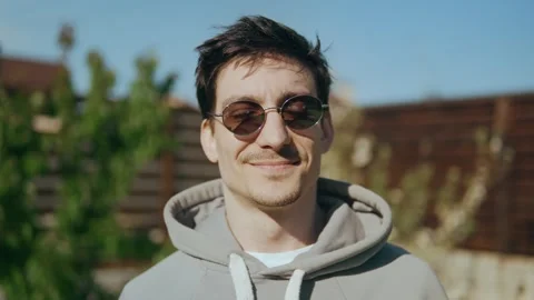 Guy in sunglasses looks at the camera and smiles enjoying the rays of the sun Stock Footage 247359992