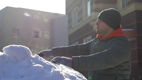 A guy sweeps fresh snow from his car with a brush after a blizzard on a bright Stock Footage 160987635