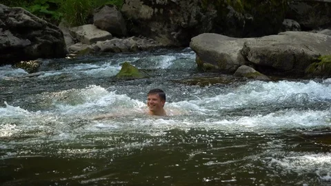 The guy is swimming in the river. A young cute guy bathes in a clean mountain Stock Footage 95283083