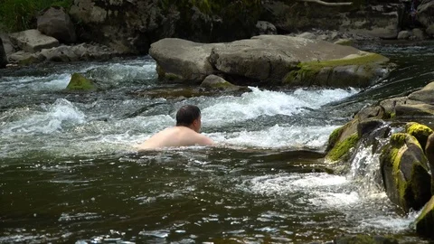 The guy is swimming in the river. A young cute guy bathes in a clean mountain Stock Footage 95283287