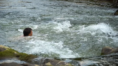 The guy is swimming in the river. A young cute guy bathes in a clean mountain Stock Footage 95283437