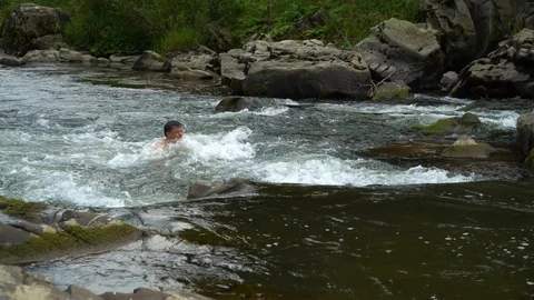 The guy is swimming in the river. A young cute guy bathes in a clean mountain Stock Footage 95283833