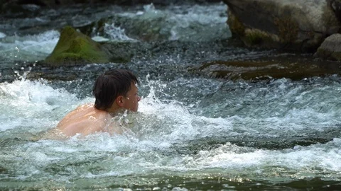 The guy is swimming in the river. A young cute guy bathes in a clean mountain Stock Footage 95394357