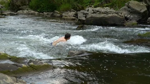 The guy is swimming in the river. A young cute guy bathes in a clean mountain Stock Footage 95394580