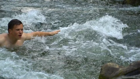 The guy is swimming in the river. A young cute guy bathes in a clean mountain Stock Footage 95394878