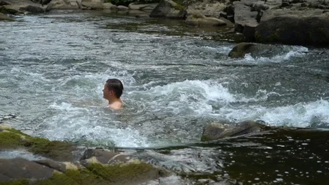 The guy is swimming in the river. A young cute guy bathes in a clean mountain Stock Footage 95395072