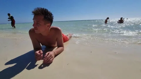 A guy in swimming trunks is lying on the shore of the sea Stock Footage 237592783