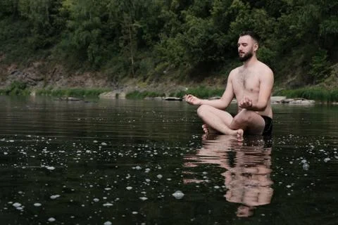 A guy in swimming trunks sits on the surface of the water in a river or lake Stock Photos