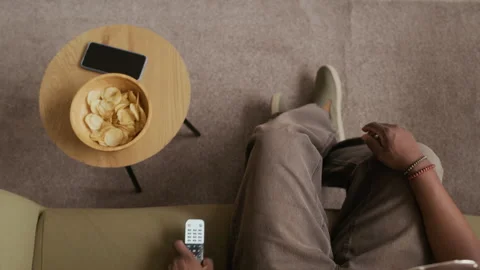 Guy Switching on TV, Taking Potato Chips and Checking Messages in Smartphone Video stock 316919498