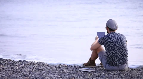 A guy with a tablet sitting on the beach 스톡 동영상 58219038