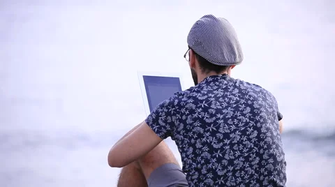A guy with a tablet sitting on the beach 스톡 동영상 58221382