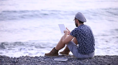 A guy with a tablet sitting on the beach 스톡 동영상 58224800