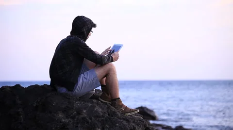 A guy with a tablet sitting on the rock Stock Footage 58116724