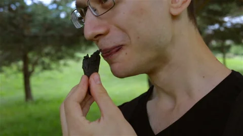 The guy takes a bite of his black ice cream cone. Female hand appears in the fra Stock Footage 102156034