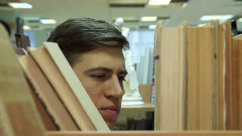 The guy takes the book from the shelf, close-up of the face and the book 스톡 동영상 155962836