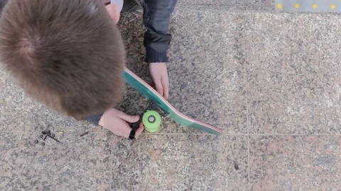 Guy takes the key in his hand and begins to twist the bolts on the skateboard Video stock 80560497