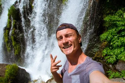 The guy takes a selfie against the backdrop of a waterfall. Travel blogger. Stock Photos