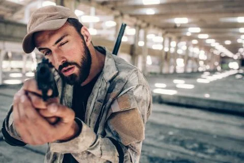 Guy is taking aim. He is looking straight forward on camera. He wears military 库存照片
