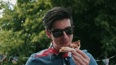 Guy taking a bite of pizza at independence day party Stock Footage 133607814