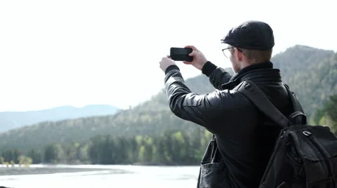 Guy taking photo on his mobile phone camera of a beautiful landscape Stock Footage 63385128