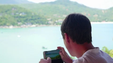 Guy is taking pictures on a smartphone panoramic view of the sea and mountains Vidéo 74762717