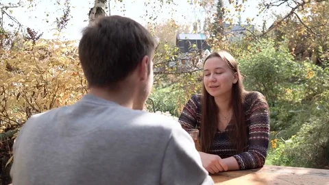 Guy talking with a girl sitting on the veranda in front of the house and drinkin Stock Footage 80237139