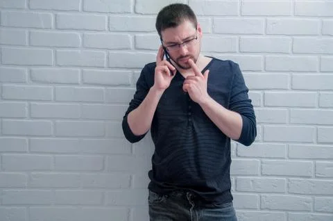 The guy is talking on the phone on the background of a white loft. Stock Photos
