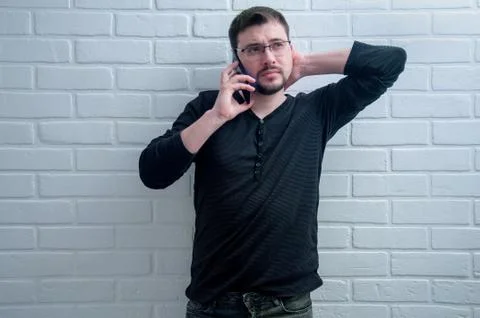 The guy is talking on the phone on the background of a white loft. Stock Photos