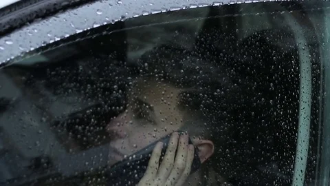 The guy is talking on the phone in the car in the rain. Behind the glass. Stock-Footage 75207062