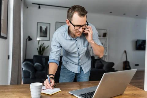A guy is talking on phone, using laptop 스톡 사진