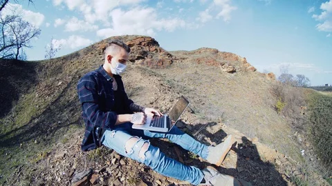 Guy talking on video calling on a laptop in a medical mask away from the city Stock Footage 128432624