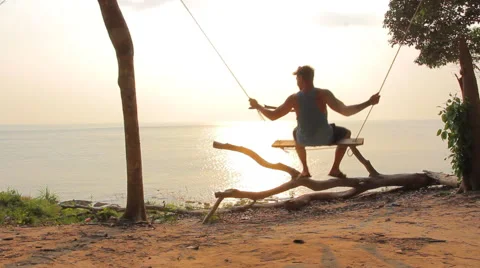The guy with tattoo on his shoulder going on the swings at the seaside Stock Footage 64207157