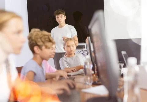 Guy teacher teaches group of students in computer class Stock Photos