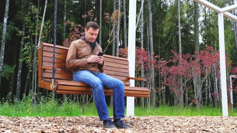 Guy texting on mobile phone in park. Young caucasian man relaxing on wooden Stock Footage 168401356