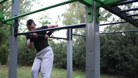 Guy trains calisthenics on pull up bar in outdoor gym wearing sports gear focusi Video stock 316701422