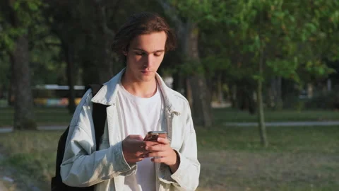 Guy is typing a text message on a mobile phone. Young man is walking outdoors Stock Footage 219934324