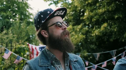Guy with USA hat talking and shaking his head outdoors at 4th of July Party Stock Footage 133613922