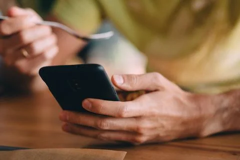 Guy using phone while eating, close view of hands using black phone Stock Photos