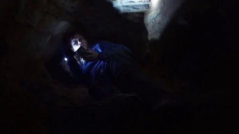 Guy using smartphone laying on ground into closely hole in cave with flashlight Stock Footage 80063339