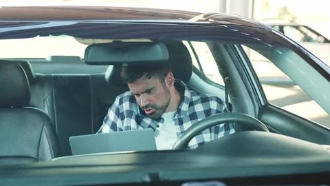 Guy using smartphone while working with laptop in the car. Slow motion Stock Photos